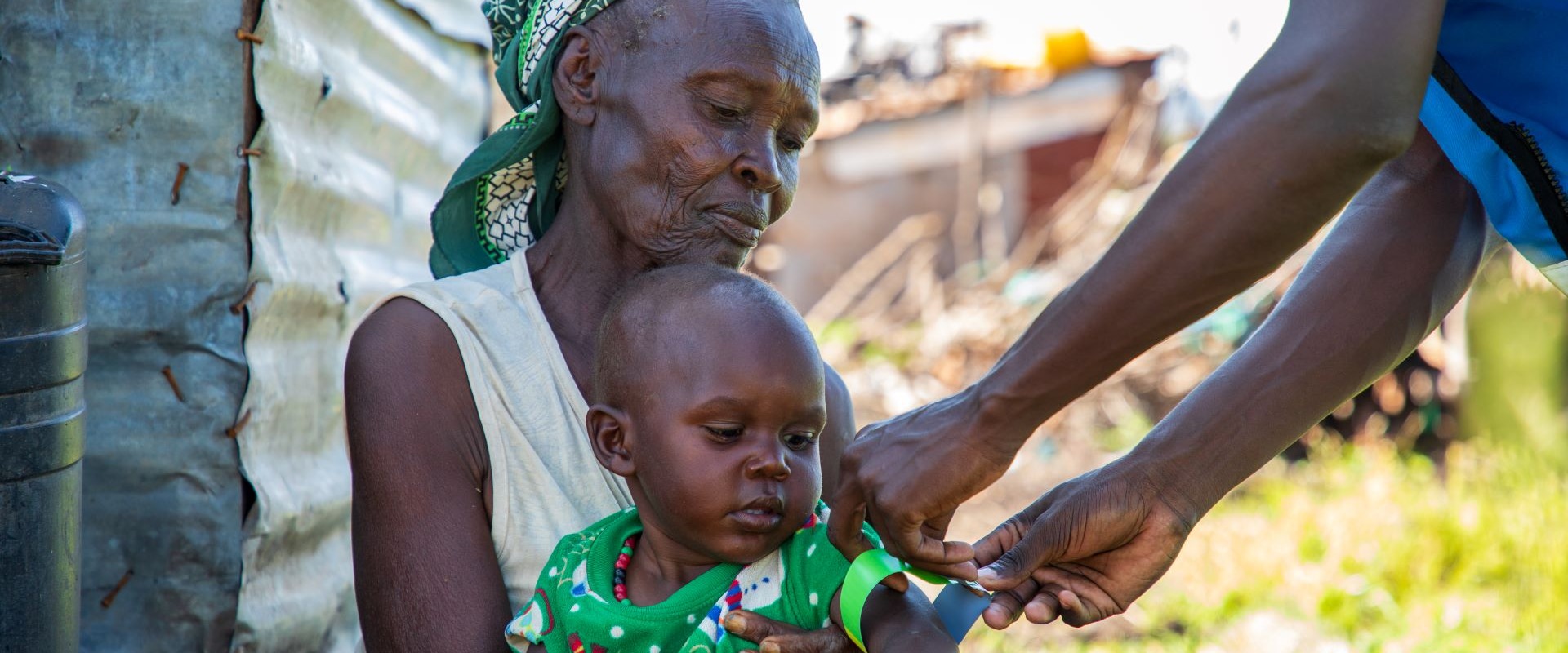 Mother holding a child while an aid worker measures the child's malnutrition level