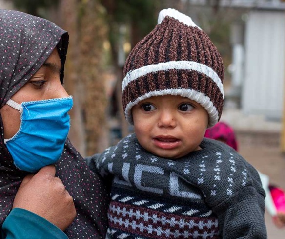 A mother, wearing a mask, holds her young son.