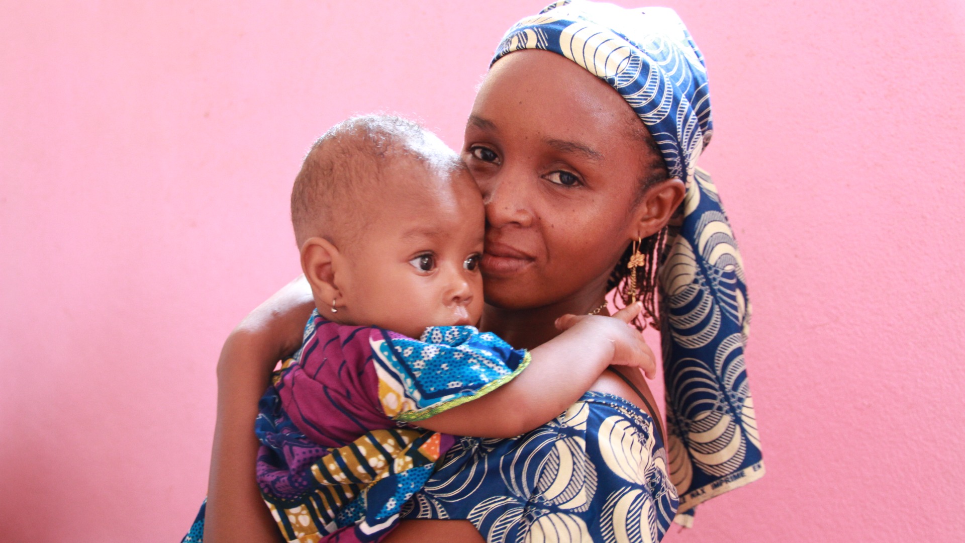 A mother and child in front of a pink wall in Cameroon.