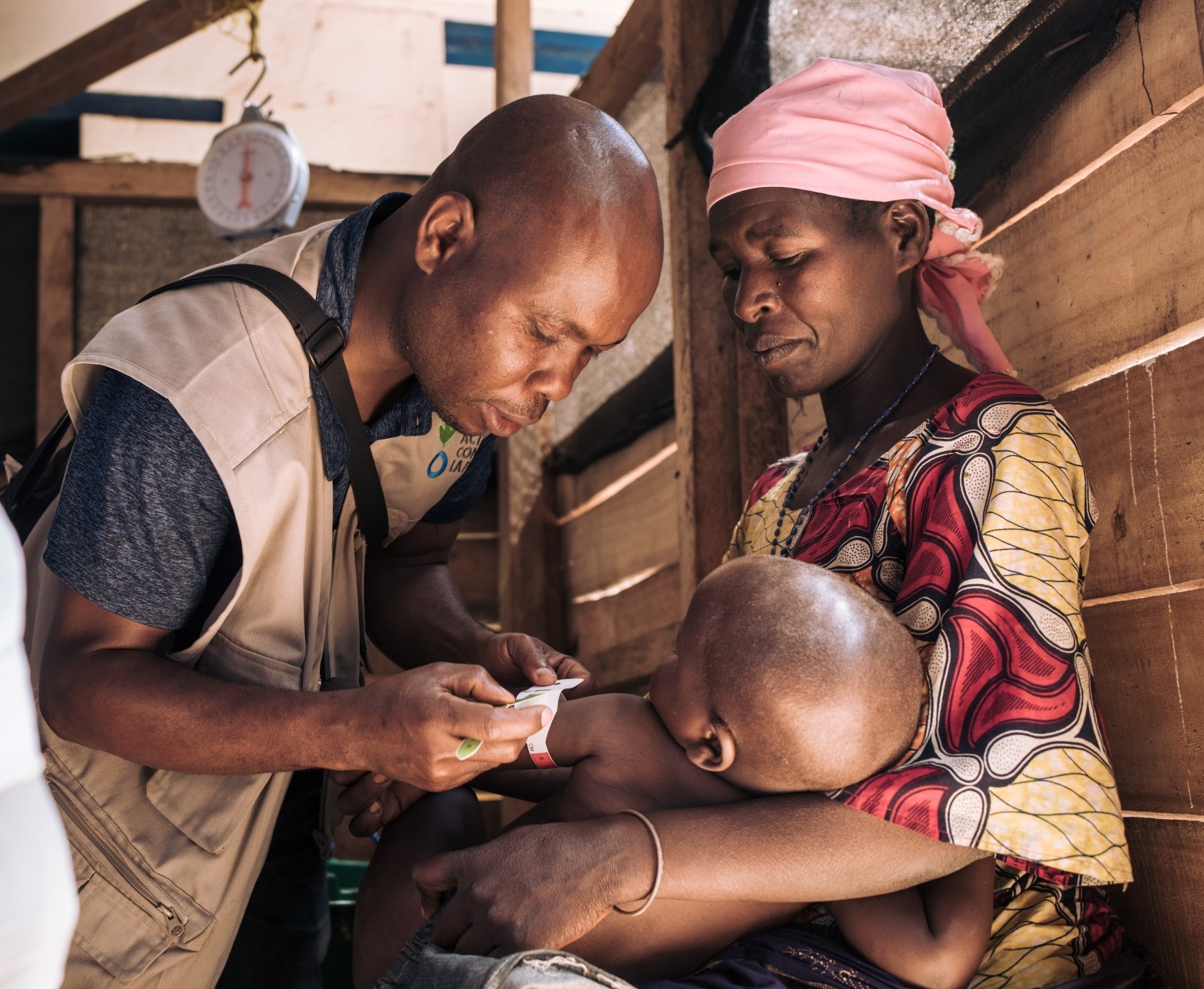 A health worker checks the nutrition status of a young boy as his mother holds him.