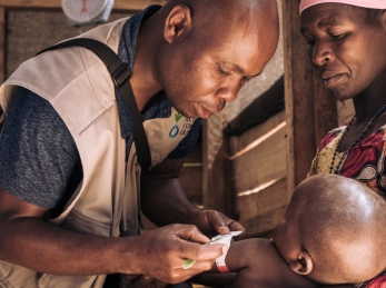 A health worker checks the nutrition status of a young boy as his mother holds him.