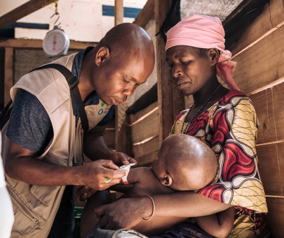 A health worker checks the nutrition status of a young boy as his mother holds him.