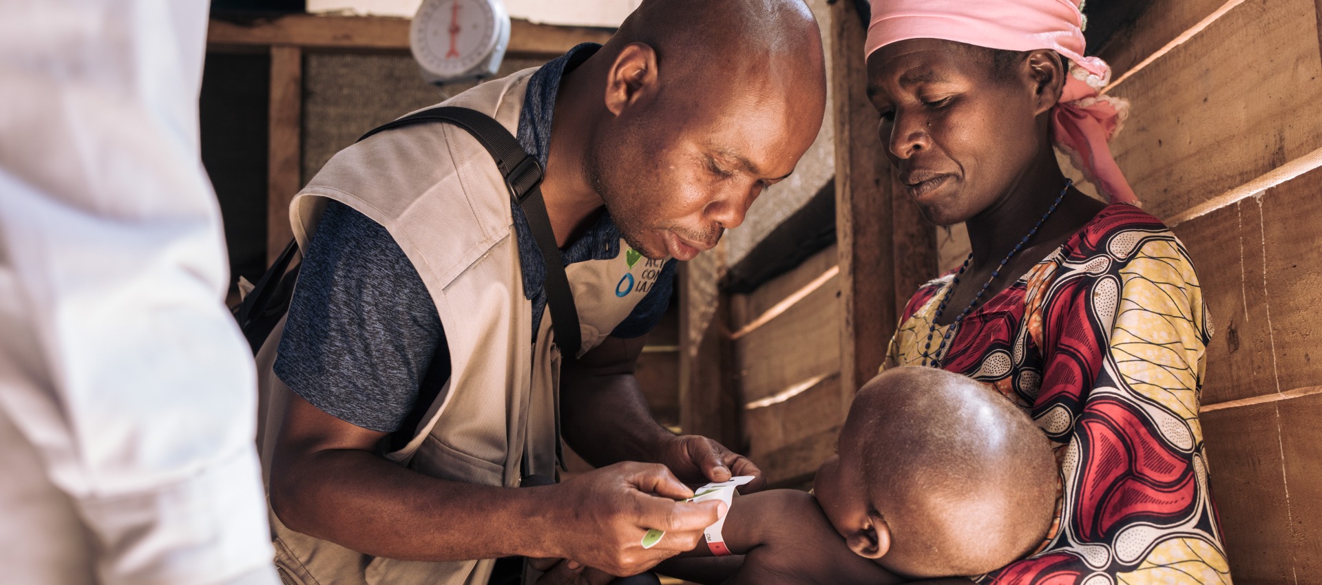 A health worker checks the nutrition status of a young boy as his mother holds him.