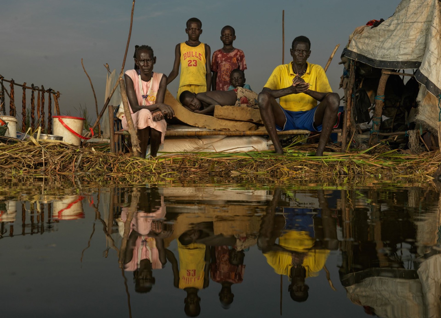 A family of six sitting on a bed surrounded by flooding in South Sudan