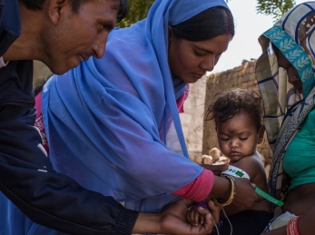 A community health worker shows a mother how to measure her child's nutrition status.