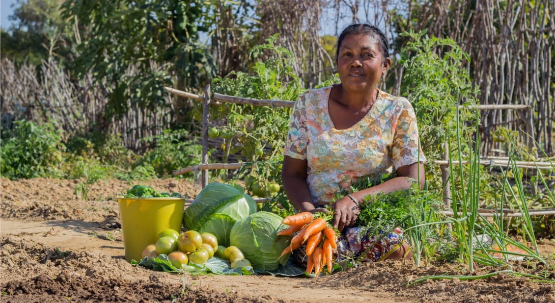 A farmer sits in her field with fresh produce.