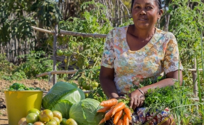 A farmer sits in her field with fresh produce.