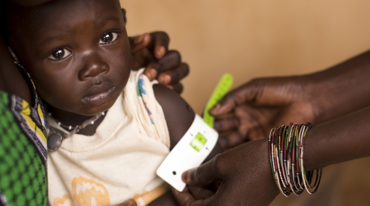 A health worker measures a child's upper arm with a color-coded band that is used to detect malnutrition.