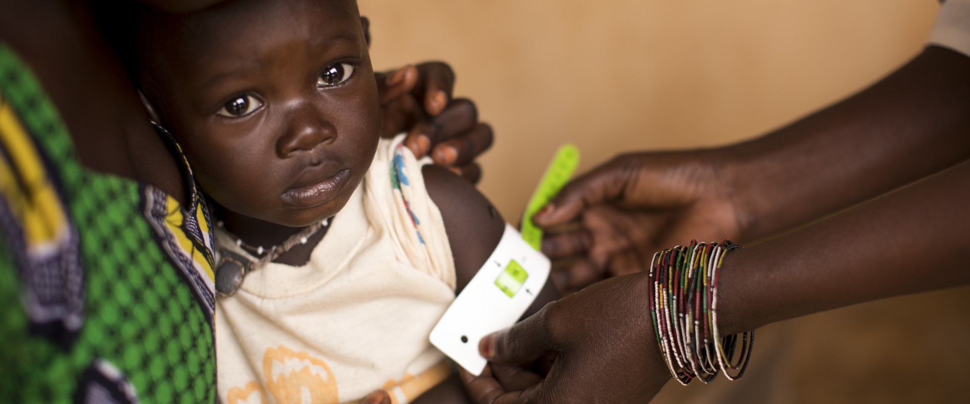 A health worker measures a child's upper arm with a color-coded band that is used to detect malnutrition.