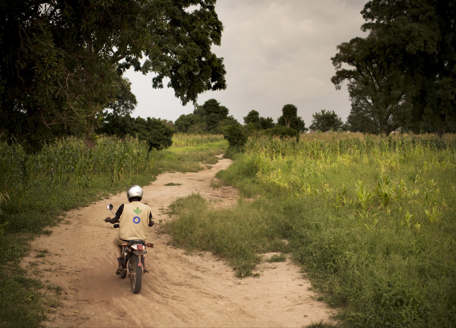 An Action Against Hunger aid worker drives a motorbike down a dirt road in Mali