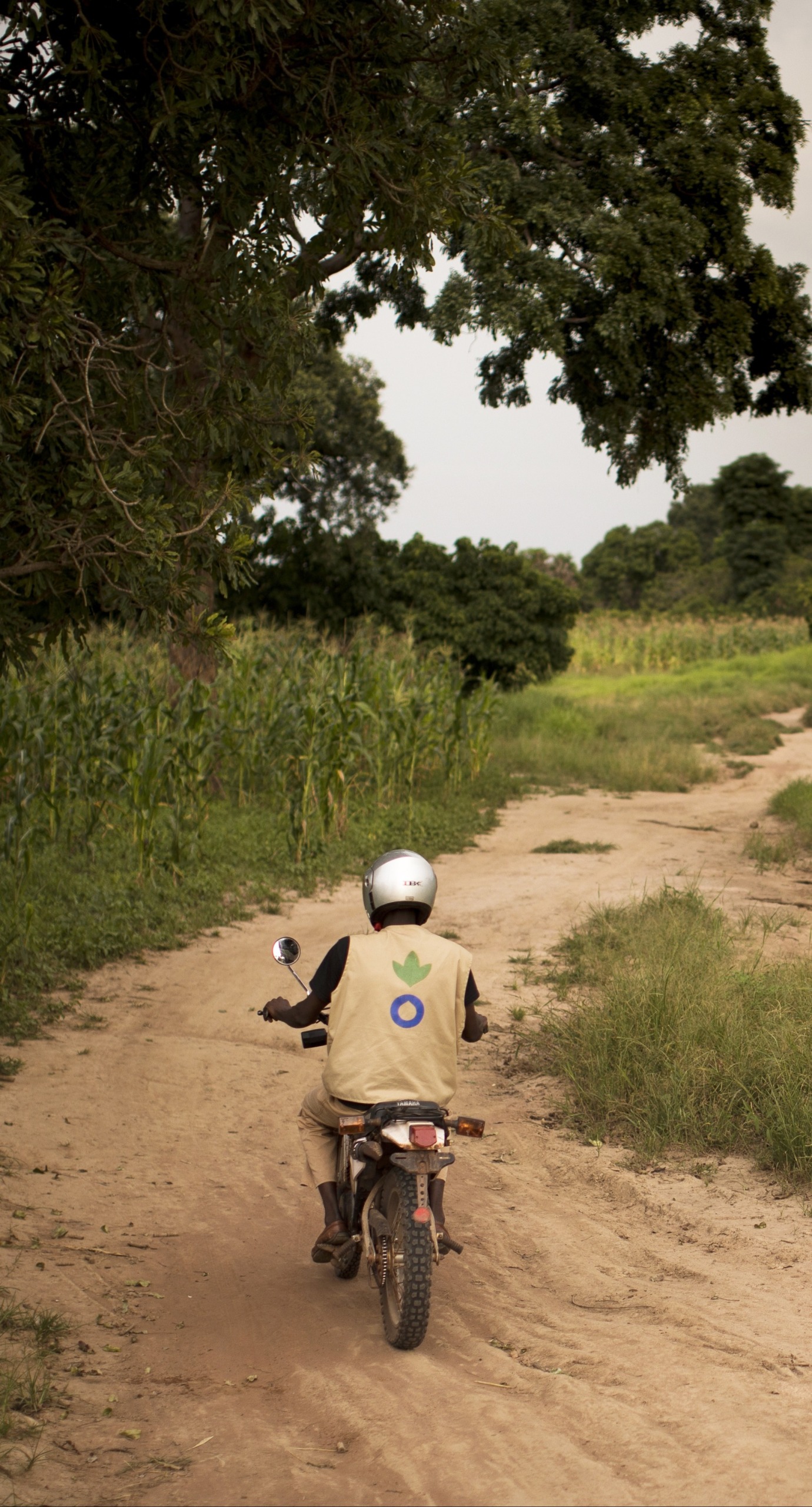 An Action Against Hunger aid worker drives a motorbike down a dirt road in Mali