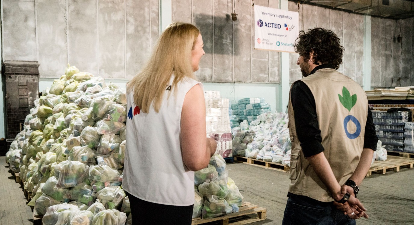 Two aid workers in a warehouse full of emergency supplies to help Ukrainian refugees.