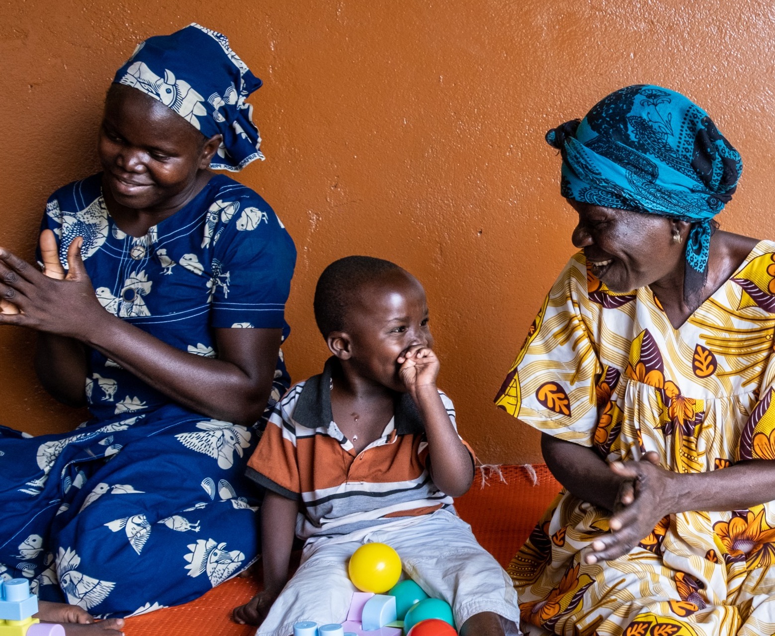 A child disabled by severe malnutrition at a young age is receiving motor skills training at the Rehabilitation center for the physically disabled (CRHAM) supported by ACF. Here, he is surrounded by the mother of another child like him and by his grandmother. Bangui, CAR. 2022