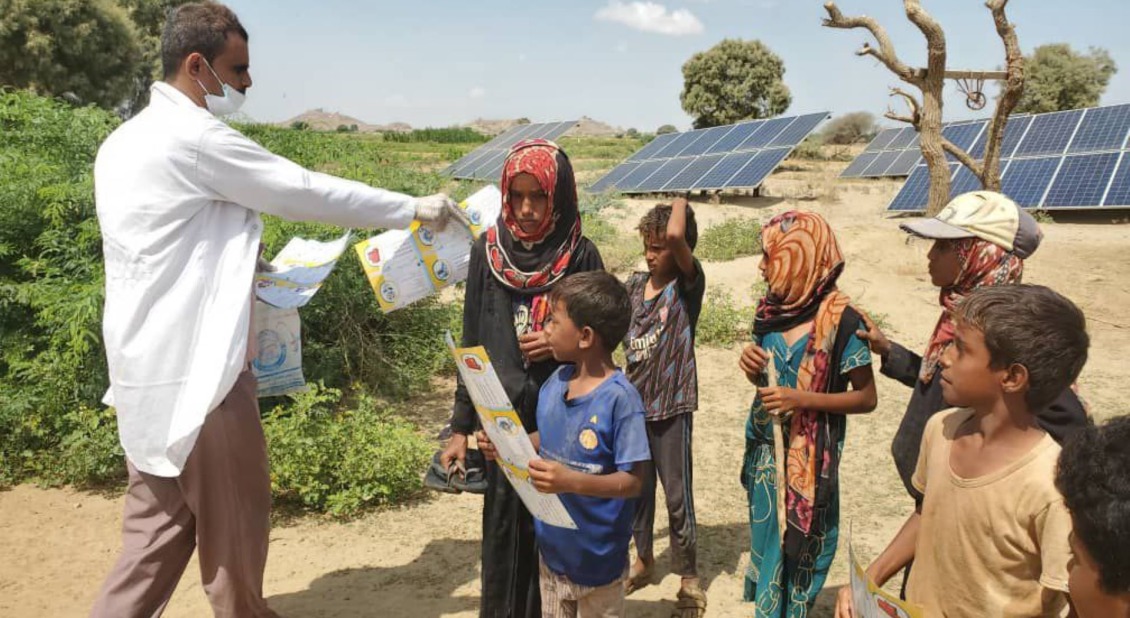 An Action Against Hunger worker hands out pamphlets to children in Yemen.