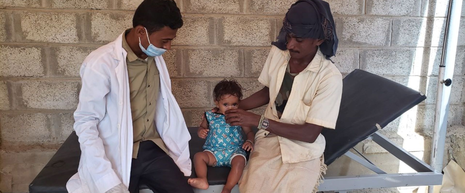 A healthcare worker helps a child next to their parent in Yemen.