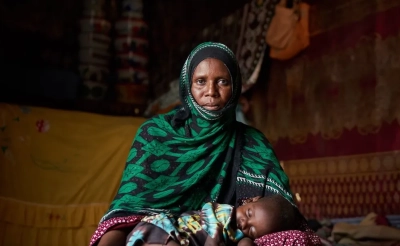A mother sits on the ground and her child lays on the ground in front of her in Chad.