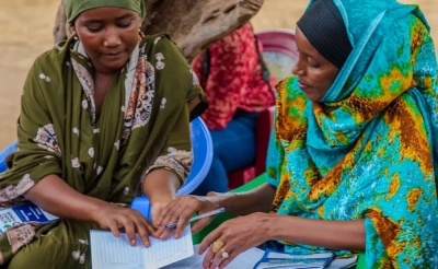 A woman training another woman with papers on thei laps in Kenya.