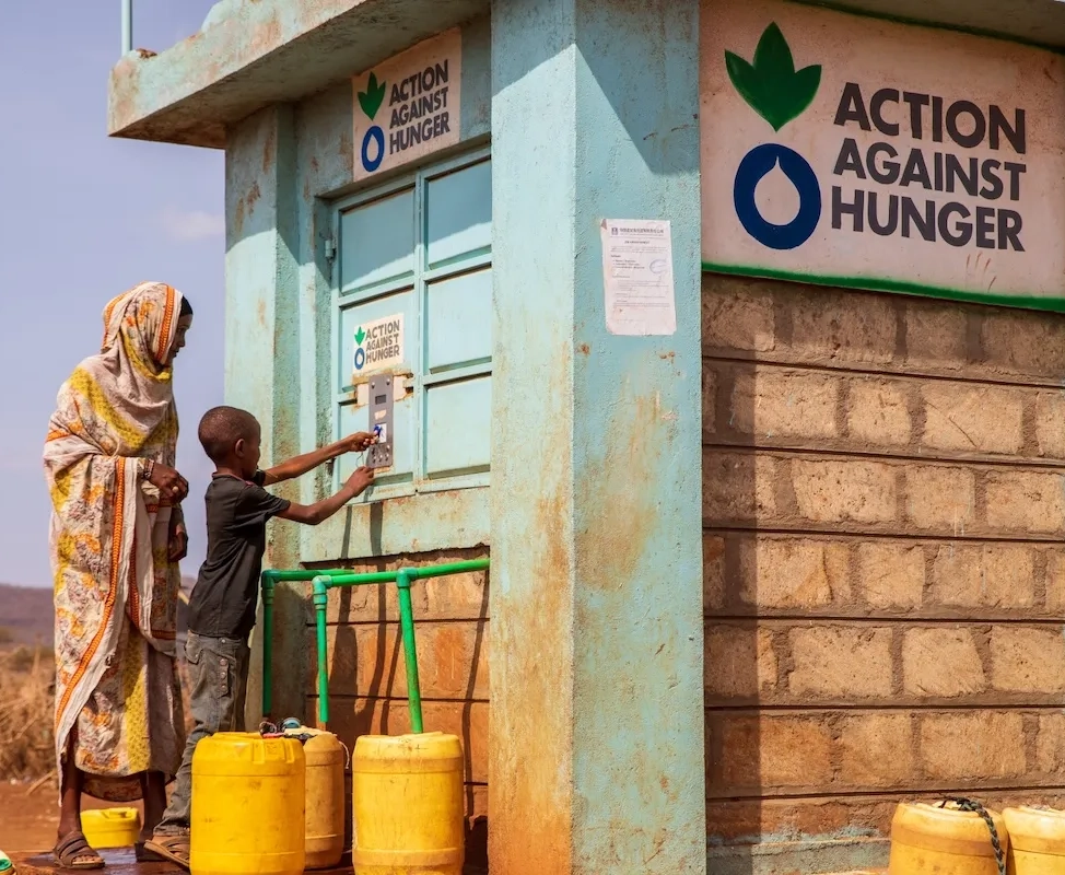 A woman and child bottling water at an Action Against Hunger Smart Tap in Kenya